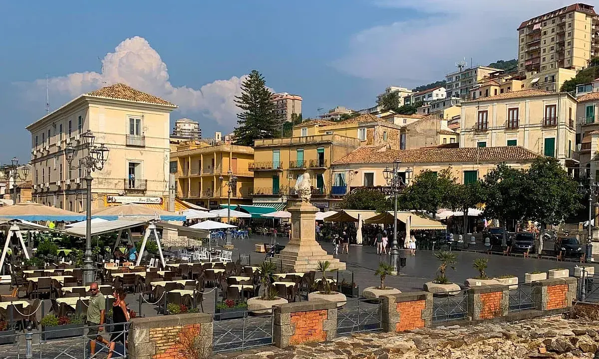 Piazza animata nel pizzo calabro centro storico, con tavoli all'aperto di ristoranti e palazzi storici sullo sfondo.