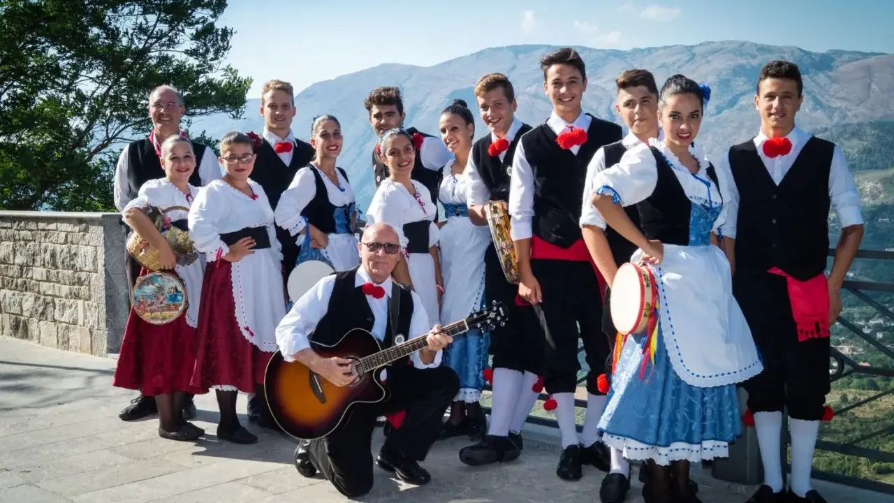 Un gruppo di persone in abiti tradizionali siciliani, pronti a intonare canzoni siciliane famose con chitarra e tamburello.