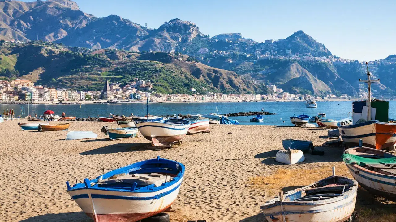 Barche da pesca sulla spiaggia di Giardini Naxos, con Taormina sullo sfondo montuoso.
