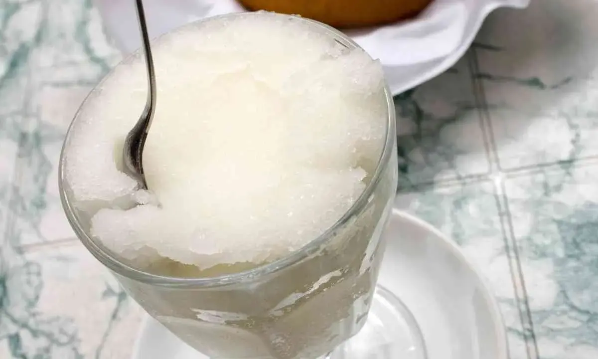 Un bicchiere colmo di granita al gelsomino, con un cucchiaino che affonda nella sua consistenza ghiacciata. Perfetta per una pausa rinfrescante.