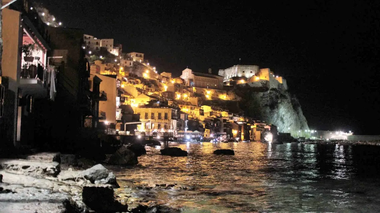 Scilla illuminata di notte, un incanto da visitare a piedi. Case colorate e il castello arroccato sul promontorio si specchiano nel mare.