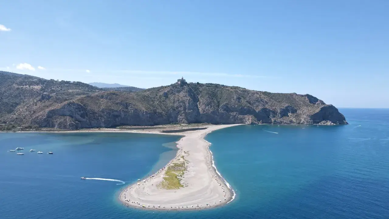 Spiaggia a forma di mezzaluna nei laghetti di Marinello, dove si può fare il bagno. Montagne verdi sullo sfondo e mare azzurro.