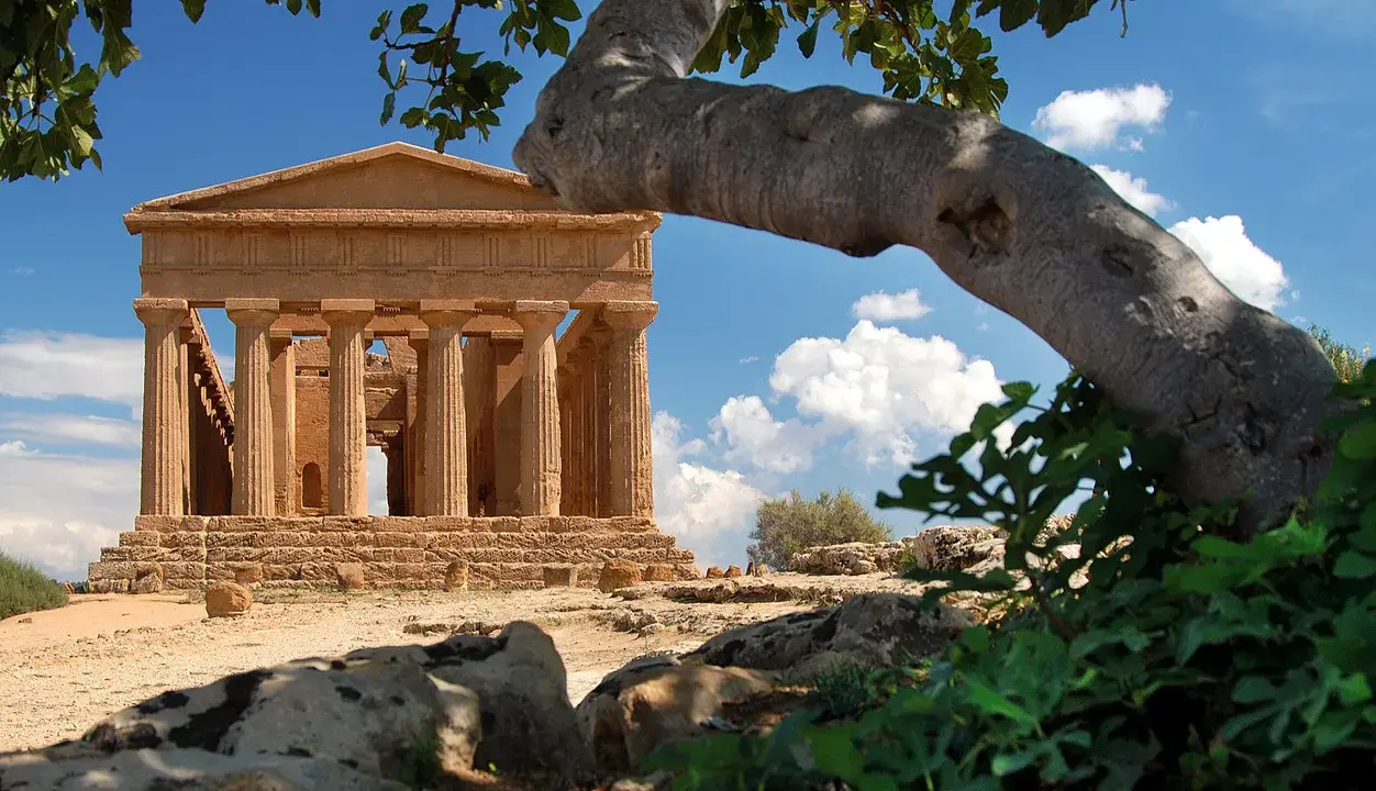 Tempio greco dorico, parte del patrimonio UNESCO Sicilia, si staglia sotto un cielo azzurro con nuvole bianche.
