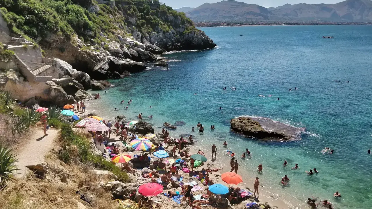 Affollata baia dei Francesi con gente che prende il sole e nuota nelle acque cristalline.