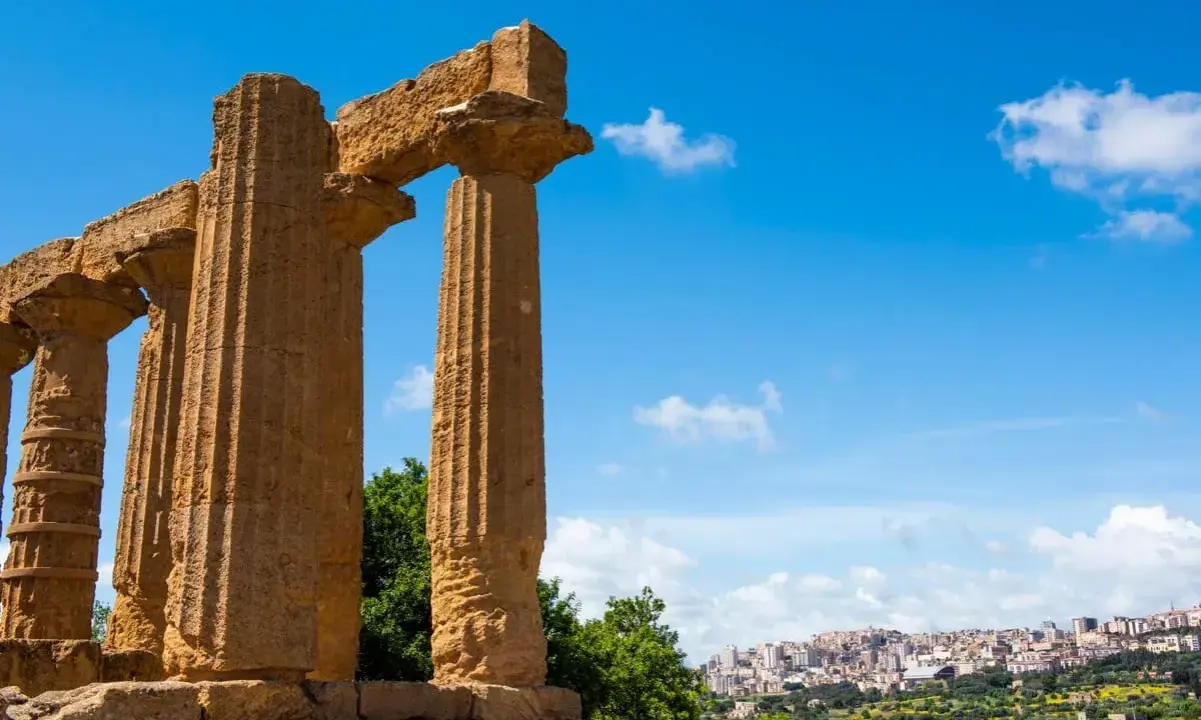 Colonne doriche imponenti, testimoni del **significato** di Akragas, con una città moderna sullo sfondo.