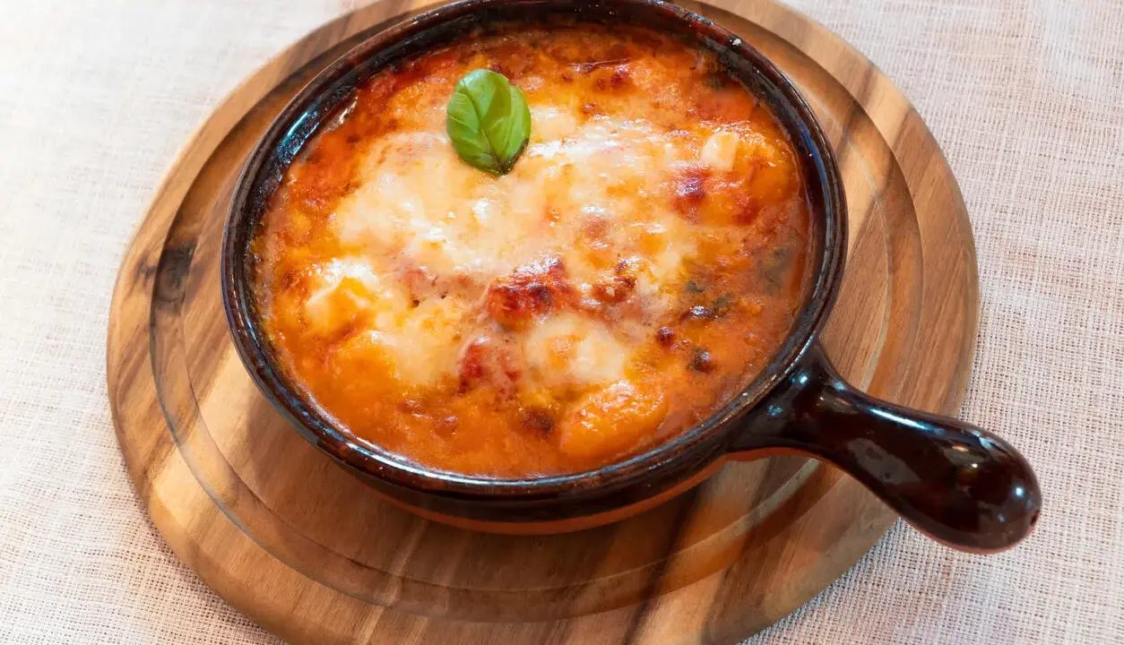Piatto fumante di gnocchi al forno, uno dei piatti tipici della Campania, con pomodoro e mozzarella filante, guarnito con basilico.