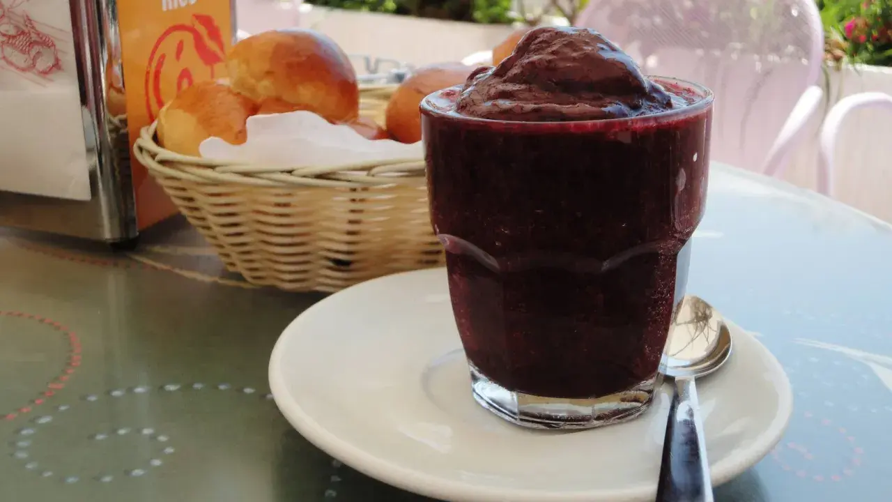 Un bicchiere di granita messinese, scura e invitante, accanto a soffici brioche in un cestino. Un'immagine che sa di sole e colazioni siciliane.