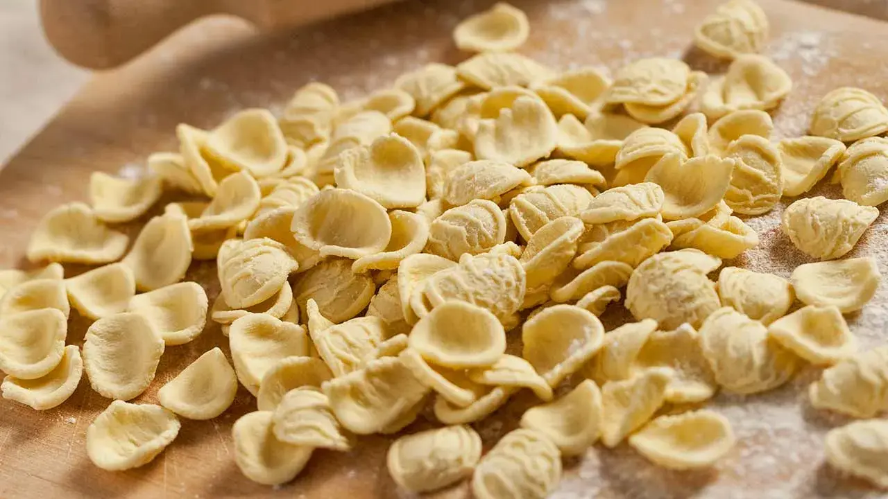 Orecchiette fresche, pronte per diventare uno dei **piatti tipici pugliesi** più amati. Un mattarello sullo sfondo evoca la tradizione.