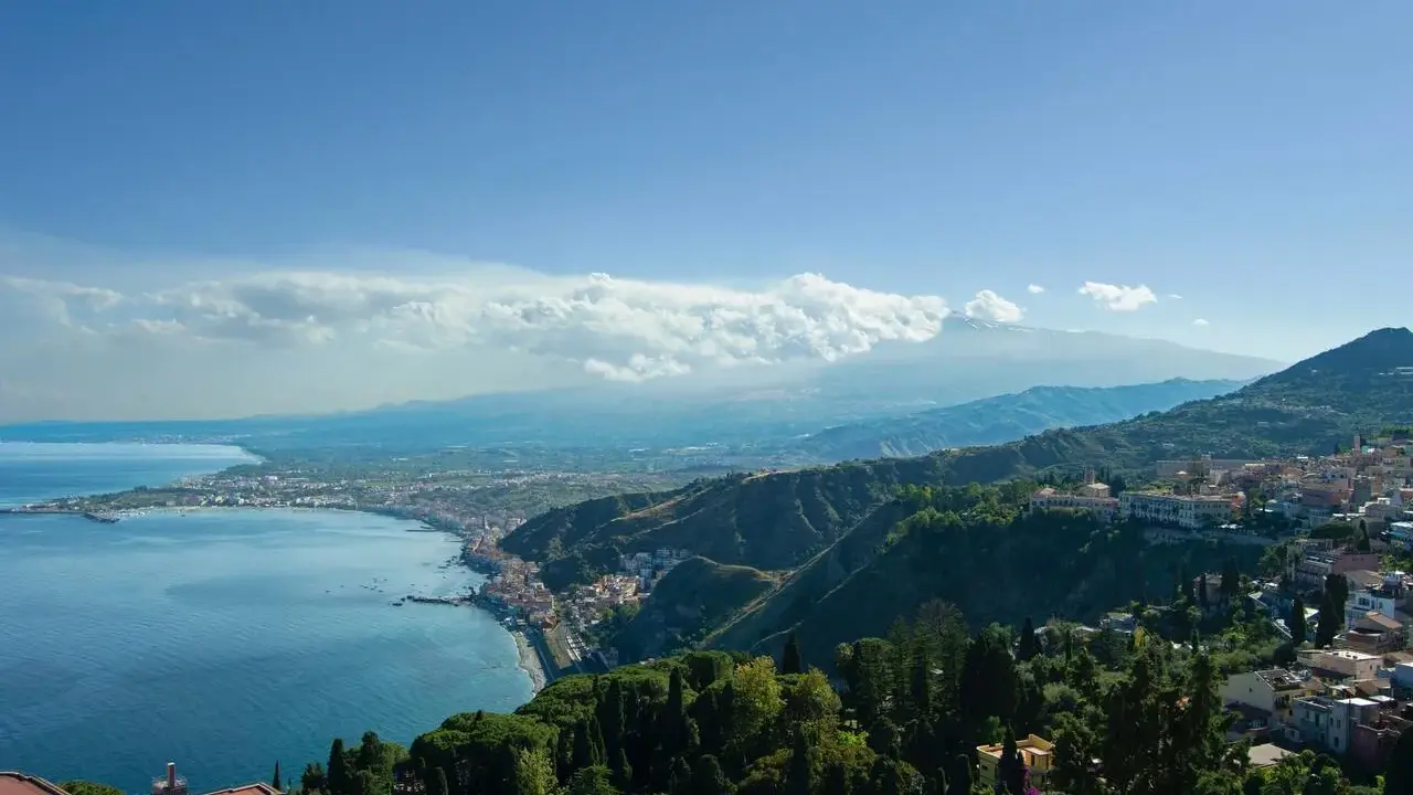 Vista panoramica della costa siciliana con il mare blu, la città di Taormina e l'Etna sullo sfondo. Un luogo incantevole, quasi un casinò di Taormina naturale.