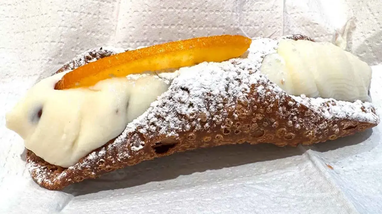 Cannolo ripieno di ricotta, uno dei dolci tipici di Palermo, cosparso di zucchero a velo e decorato con scorza d'arancia candita.