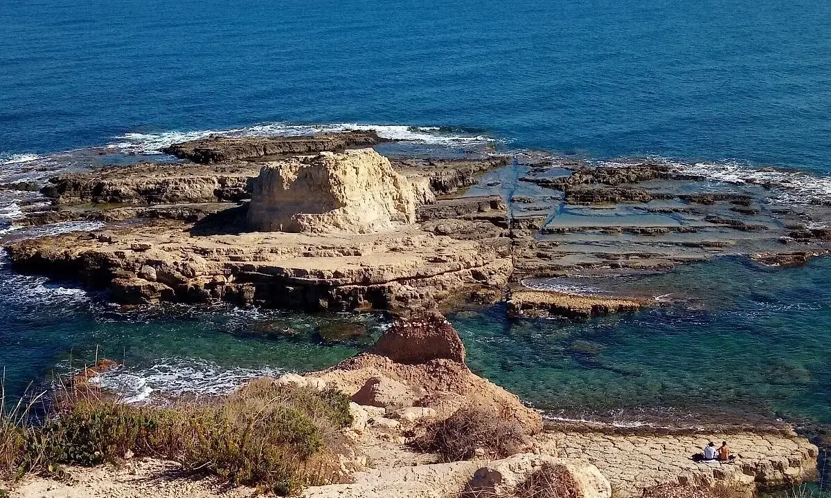 Scogliera rocciosa con acqua cristallina, dove si narra avvenne lo sbarco dei turchi. Due persone sedute ammirano il panorama.