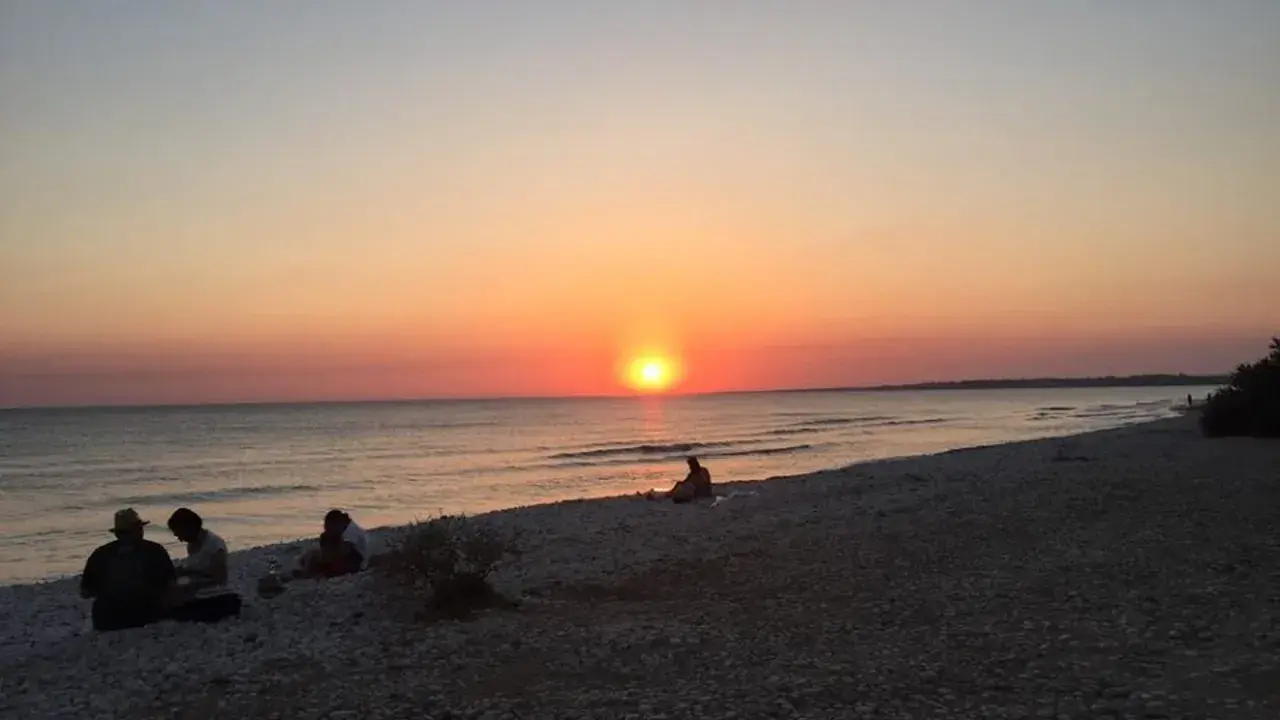 Tramonto sulle menfi spiagge più belle. Persone sedute sulla riva, godendosi la vista del sole che cala sul mare.