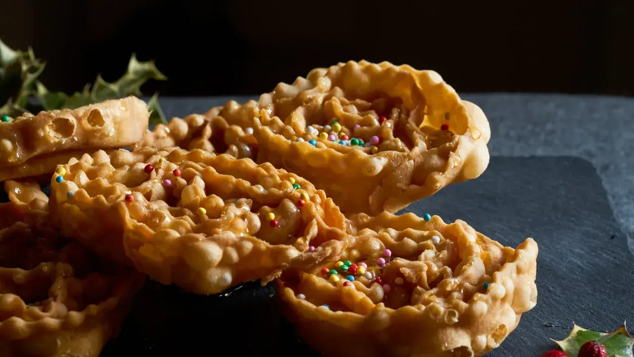 Cartellate, dolci tipici della Puglia, ricoperte di miele e confettini colorati, con un rametto di agrifoglio sullo sfondo.