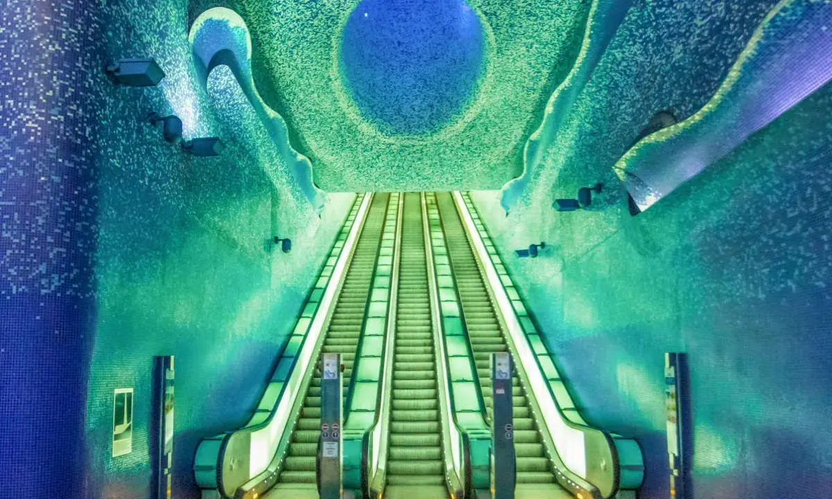 La fermata metro Napoli Toledo, famosa per la sua arte e design, con scale mobili che sembrano scendere verso un mare di mosaici blu e verdi.