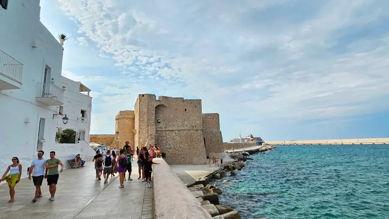 Passeggiata serale a Monopoli: il castello, il mare azzurro e una nave da crociera.