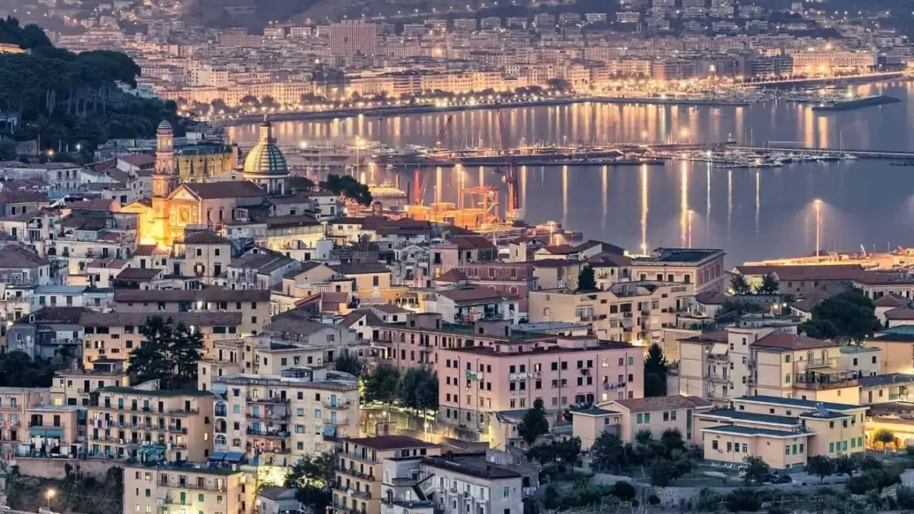 Vista notturna di un **punto panoramico Amalfi** con case illuminate e il mare scintillante.