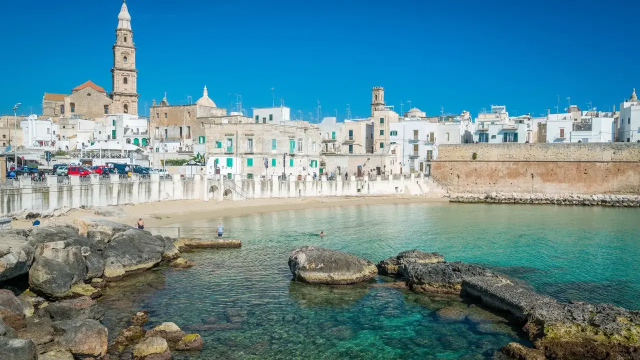 Vista del lungomare di Monopoli con case bianche, una torre campanaria e il mare cristallino. Perfetto per scoprire le cose da fare a Monopoli.