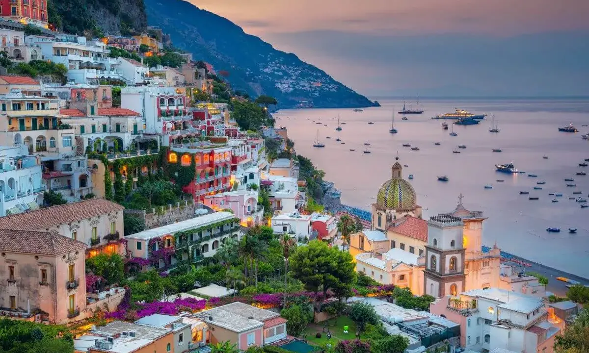 Vista mozzafiato dal **punto panoramico Positano**, con case colorate aggrappate alla scogliera e barche nel mare al tramonto.