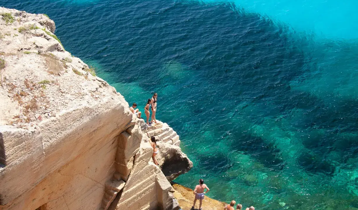 Persone si godono le splendide spiagge di Favignana, tuffandosi da scogliere in acque cristalline.