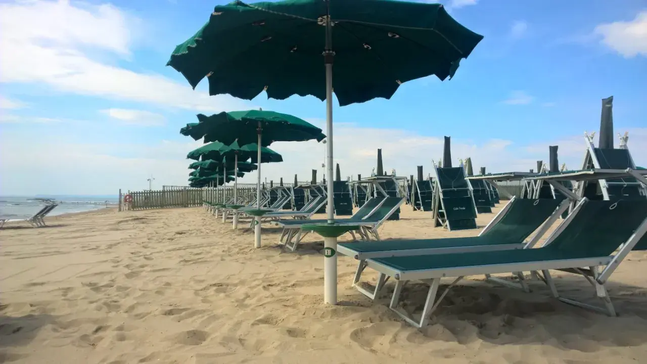 Filettato lido verde San Cataldo, con file di lettini e ombrelloni verdi sotto un cielo azzurro con nuvole bianche.