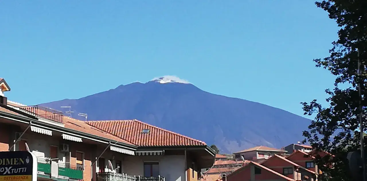 Vista dell'Etna fumante, un'imponente montagna che domina il paesaggio. Un'ottima meta per scoprire cosa vedere a Bronte, con i suoi tetti rossi in primo piano.