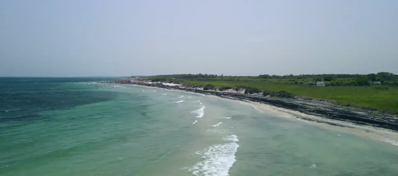Vista aerea del lido Le Cesine, con acque turchesi e una spiaggia affollata di bagnanti e ombrelloni rossi.