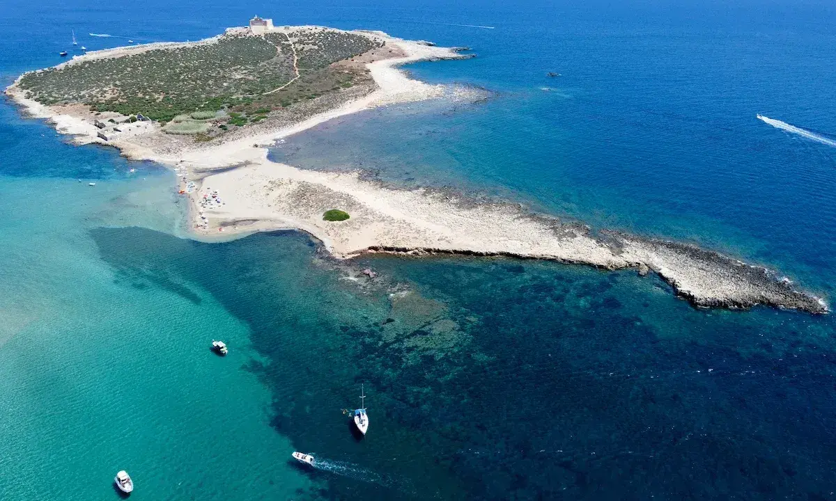 L'isola delle Correnti, leggenda di sabbia e mare cristallino, con un faro bianco e barche che solcano le acque turchesi.
