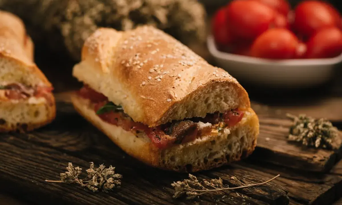 Panino con pomodoro e acciughe, un classico della cucina povera siciliana, su tagliere in legno con erbe aromatiche.