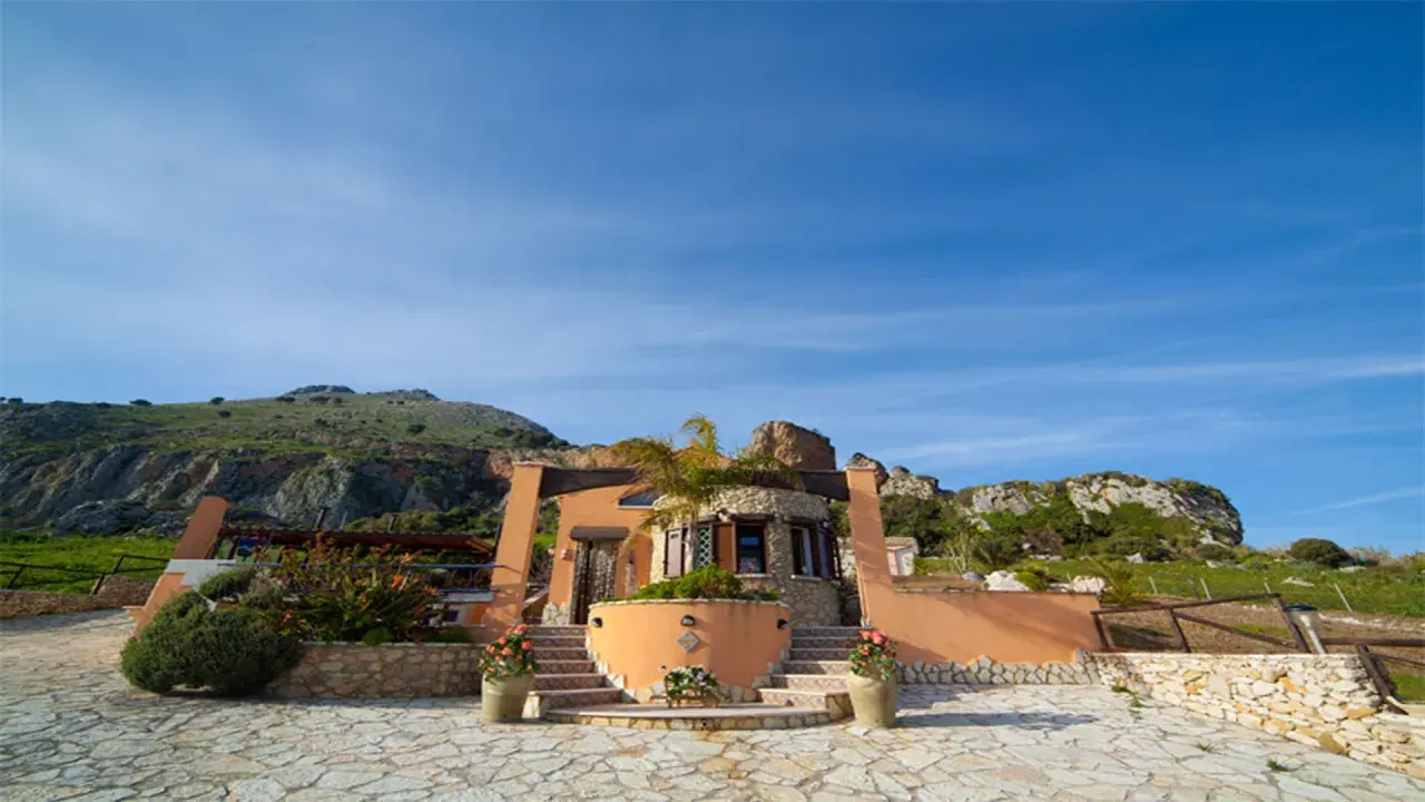 Il castello di Baida, con la sua architettura unica, si erge su un terreno roccioso sotto un cielo azzurro.