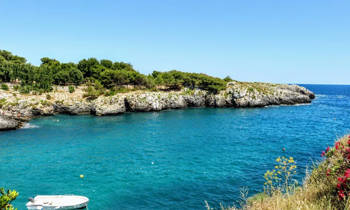 Acque cristalline e scogliere rocciose, un angolo di paradiso tra le spiagge Salento. Una piccola barca bianca galleggia tranquilla.