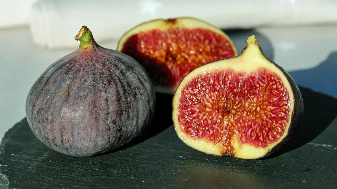 Un intero fico viola e due metà succose rivelano la dolcezza di una varietà di fichi siciliani, con la loro polpa rossa e i semi dorati.