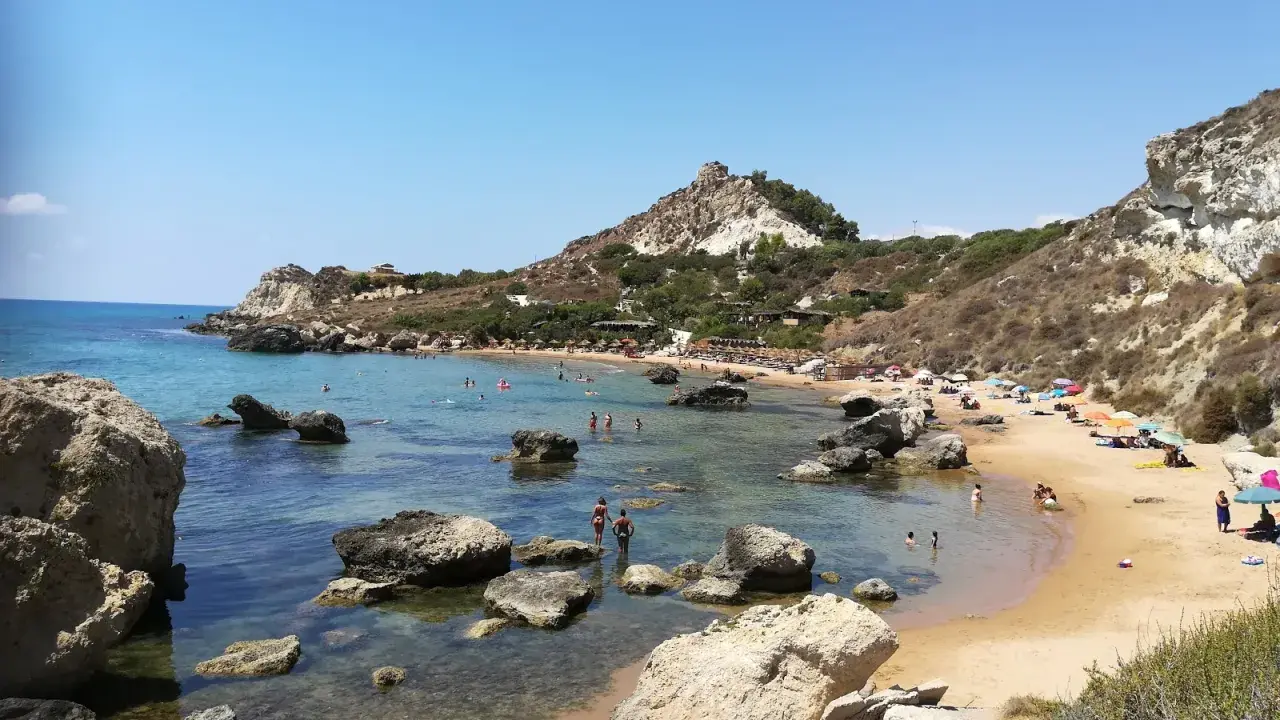 Splendida spiaggia la rocca licata con acque cristalline e scogliere rocciose. Turisti si godono il sole e il mare.