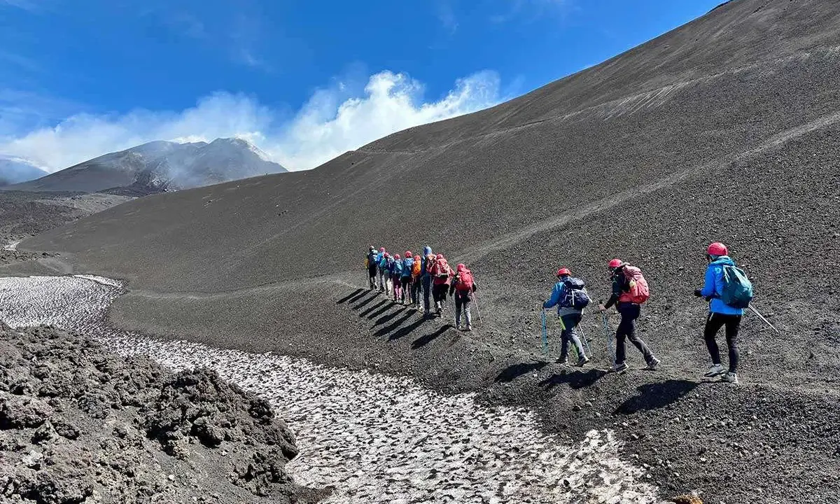 Escursionisti sul fianco di quello che i siciliani chiamano l'Etna, con fumo che sale dalla cima.