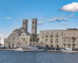 Molfetta cosa vedere: la Basilica e il porto con pescherecci sotto un cielo azzurro e nuvoloso.