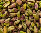 Un mucchio di pistacchi, alcuni con il guscio screpolato che rivela il loro interno verde brillante, ricordano il sapore del pistacchio in siciliano.