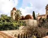 Le iconiche cupole rosse di Palermo si stagliano tra palme e vegetazione lussureggiante, un'antica bellezza sotto un cielo nuvoloso.