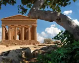 Tempio greco dorico, parte del patrimonio UNESCO Sicilia, si staglia sotto un cielo azzurro con nuvole bianche.
