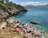 Affollata baia dei Francesi con gente che prende il sole e nuota nelle acque cristalline.