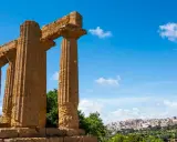 Colonne doriche imponenti, testimoni del **significato** di Akragas, con una città moderna sullo sfondo.