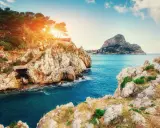 Scogliere rocciose e mare blu intenso vicino a Milazzo, con sentieri che scendono verso l'acqua. Le spiagge di Milazzo offrono panorami mozzafiato.