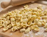 Orecchiette fresche, pronte per diventare uno dei **piatti tipici pugliesi** più amati. Un mattarello sullo sfondo evoca la tradizione.