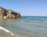 Spiaggia di Eloro con scogliere rocciose, mare azzurro e una persona che fa il bagno.