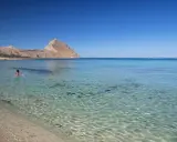 Bambina su un materassino rosa galleggia nelle acque cristalline della macari spiaggia, con montagne sullo sfondo.