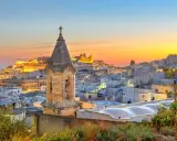 Campanile in primo piano, sullo sfondo la città bianca di Ostuni illuminata dal tramonto. Perfetto per scoprire cosa vedere a Ostuni in mezza giornata.
