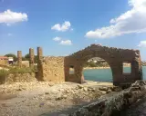 Rovine di una tonnara ad Avola, con un arco in pietra che si affaccia su una spiaggia affollata e il mare azzurro.