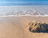 Onda che lambisce la sabbia dorata della spiaggia Tonnarella Mazara, con una roccia in primo piano.