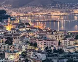 Vista notturna di un **punto panoramico Amalfi** con case illuminate e il mare scintillante.