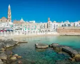 Vista del lungomare di Monopoli con case bianche, una torre campanaria e il mare cristallino. Perfetto per scoprire le cose da fare a Monopoli.