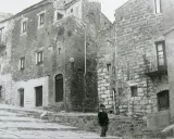 Un bambino cammina su una scalinata di pietra a Gibellina prima del terremoto. Edifici antichi in pietra la circondano.