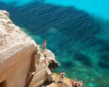 Persone si godono le splendide spiagge di Favignana, tuffandosi da scogliere in acque cristalline.